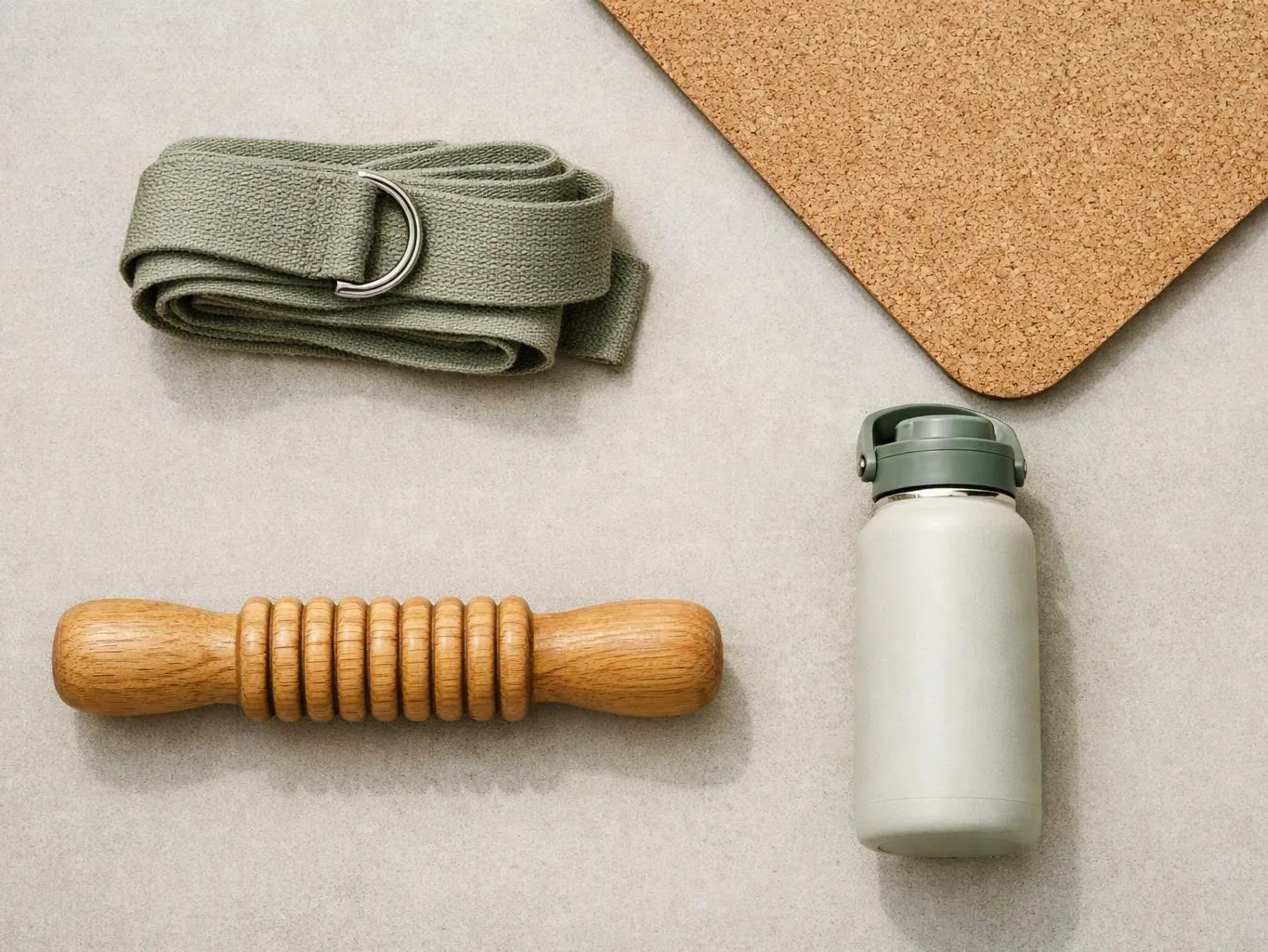 A folded green strap, wooden massage roller, water bottle, and cork mat rest on a light surface