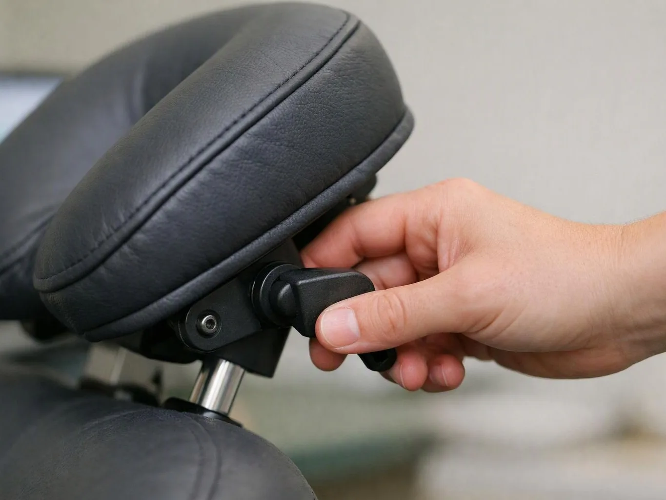 A hand adjusts a padded black headrest on a chair against a plain indoor background